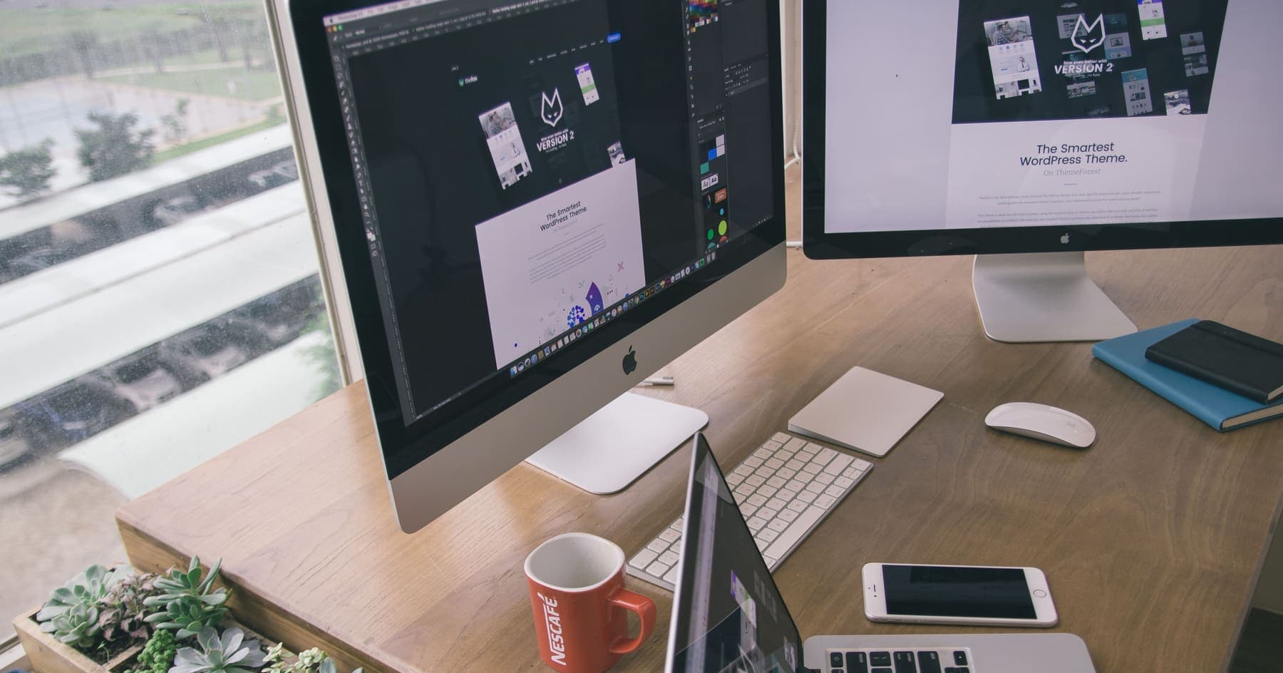 A designer's desk with a website template open across two monitors