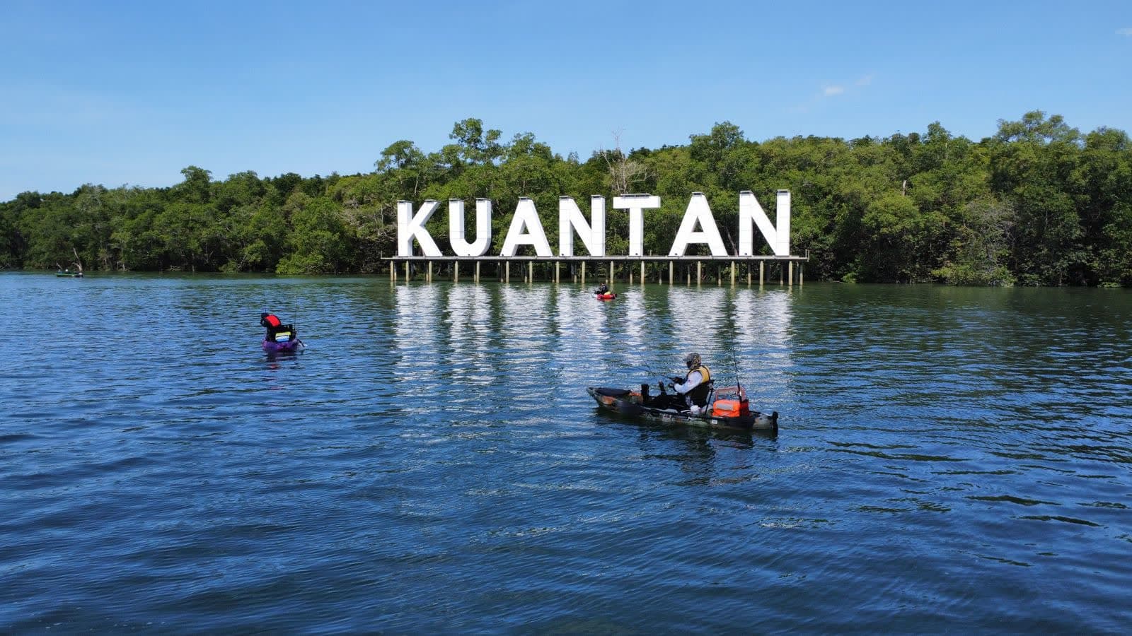 A lettered KUANTAN sign standing in the water by a mangrove shore