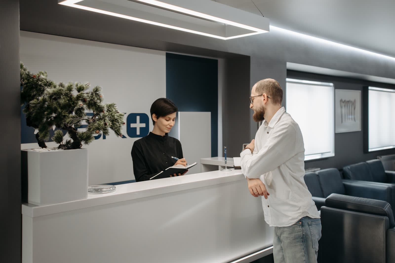 A reception counter in a clinic waiting area, staff attending a visitor