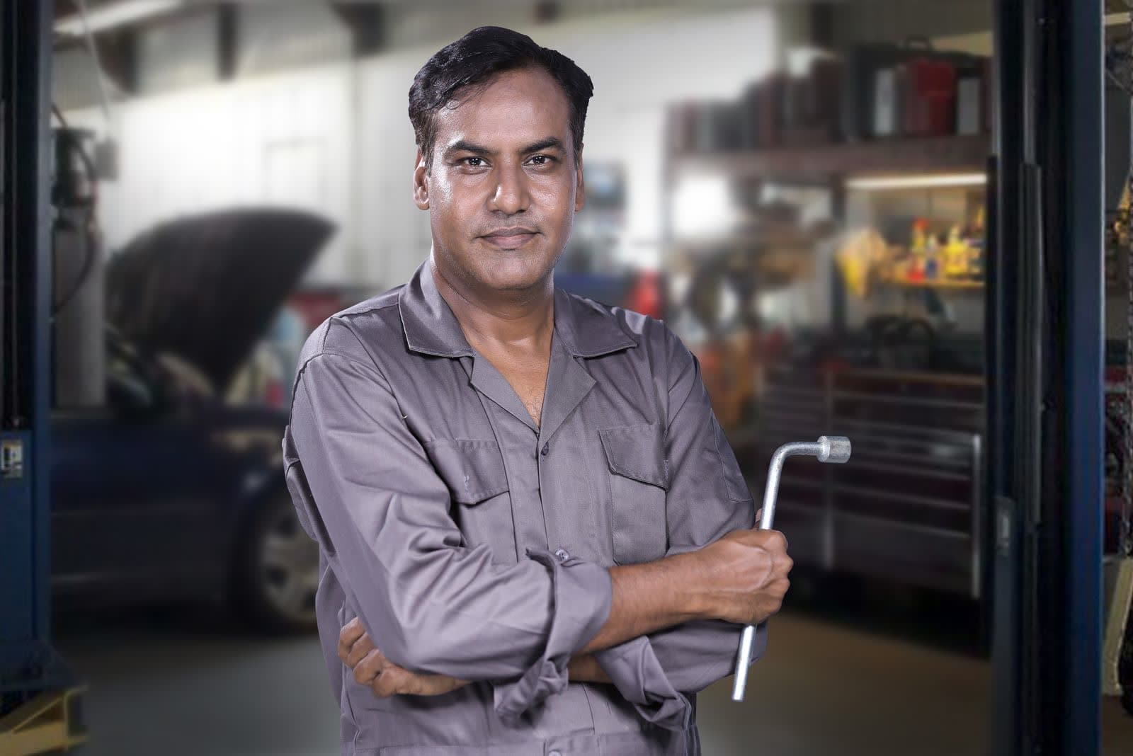 A mechanic standing in a vehicle workshop holding a spanner
