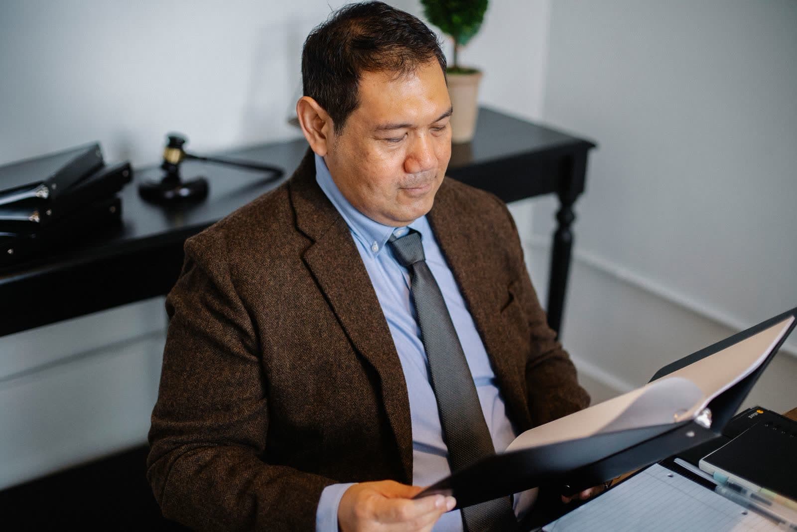 A man in a suit reading through printed documents at an office desk