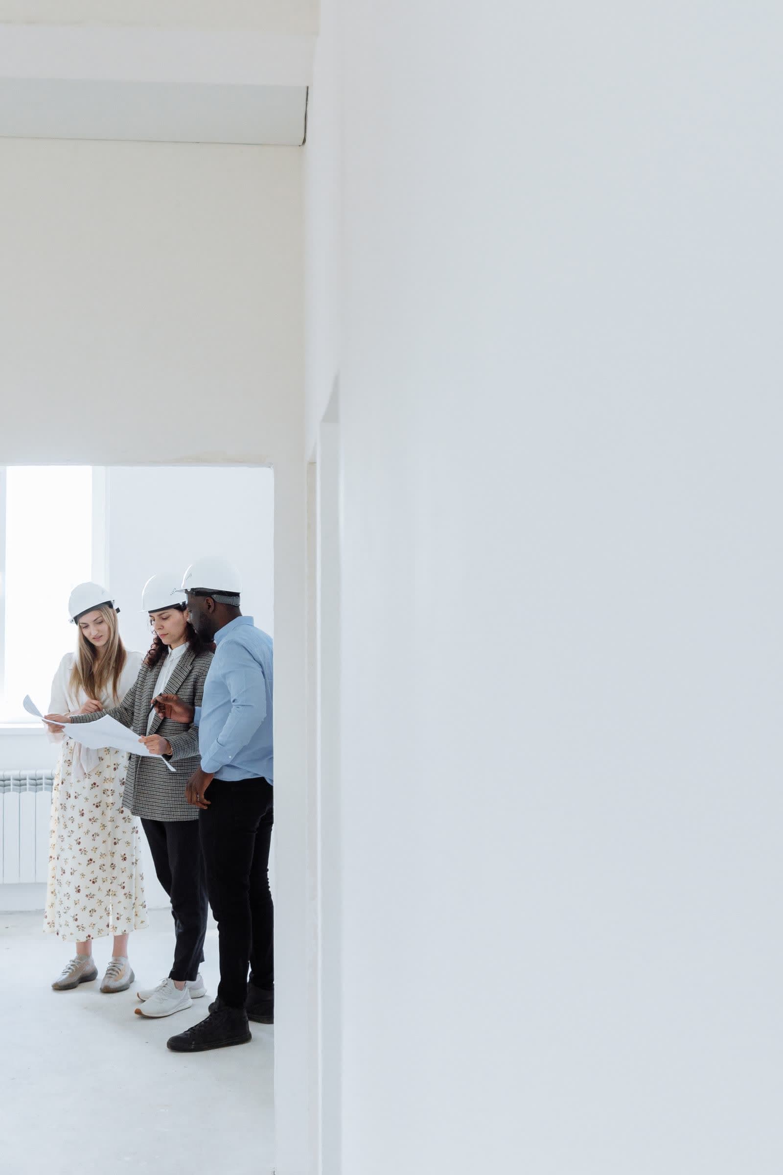 Three people in hard hats reading a drawing in an unfinished room