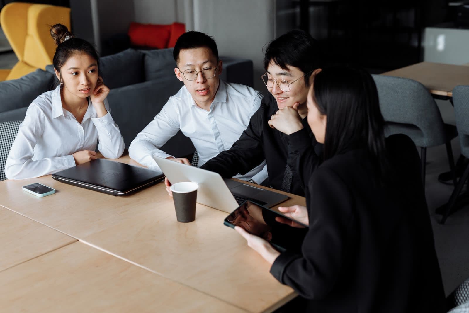 Four colleagues gathered around an open laptop at a meeting table