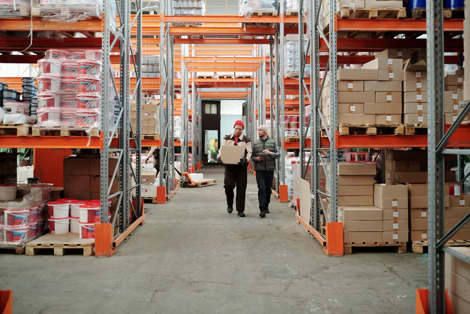 Two people walking a warehouse aisle between tall pallet racking