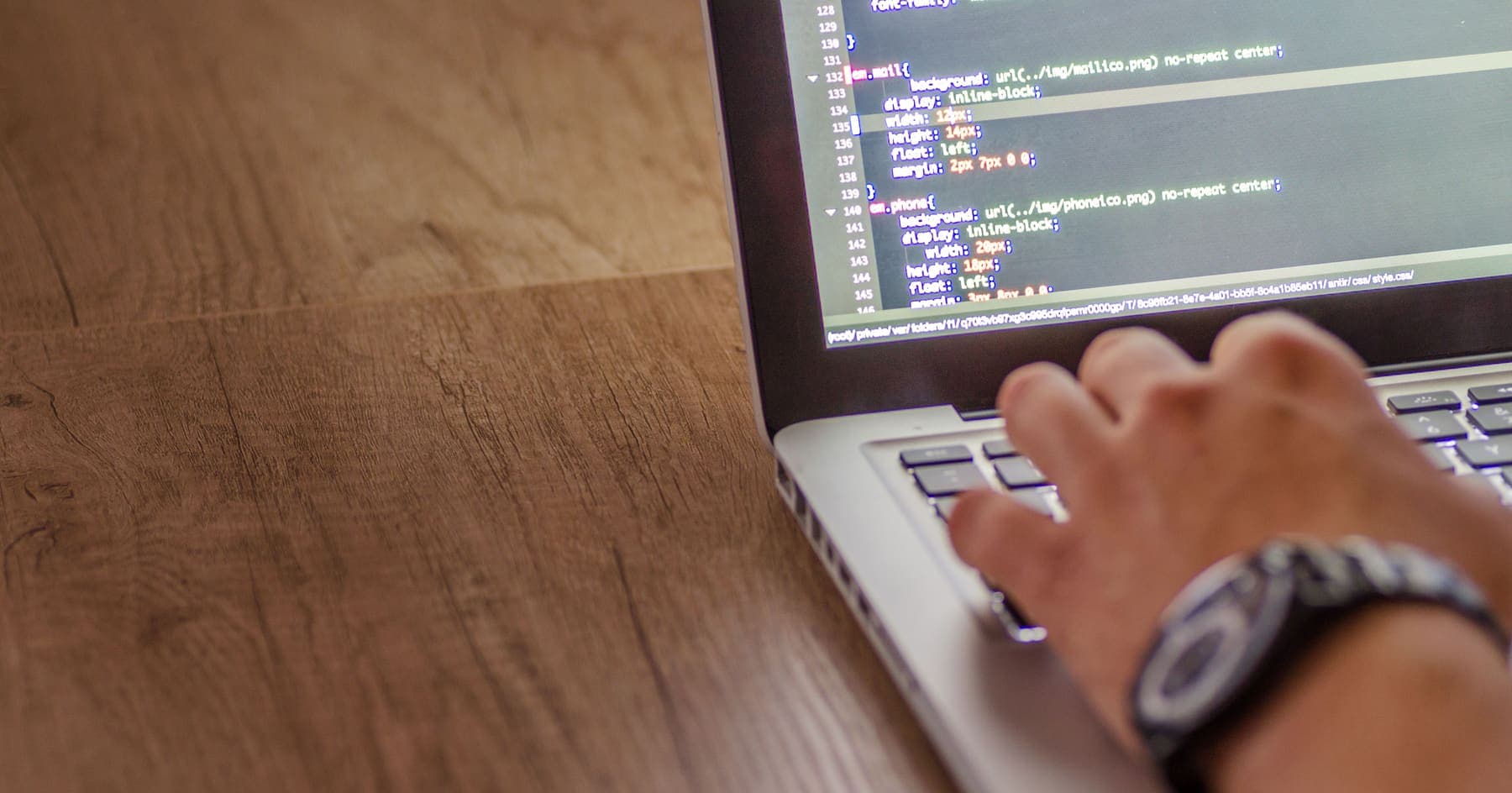 A developer's hand on a laptop keyboard with source code on screen